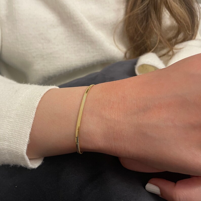May include: A gold snake chain bracelet on a person's wrist.