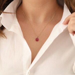 May include: A gold chain necklace with a small red flower pendant.