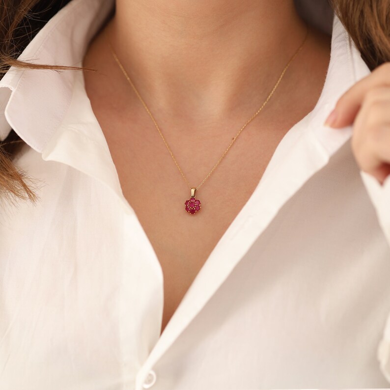 May include: A gold chain necklace with a small red flower pendant.