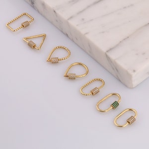 May include: A set of seven gold-toned metal clasps with different shapes, including a rectangle, triangle, teardrop, and oval. Each clasp features a decorative, clear crystal-encrusted barrel in the center. One clasp has a green crystal-encrusted barrel.