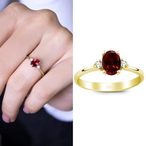 May include: A gold ring with a red oval gemstone and two smaller white gemstones on the band.