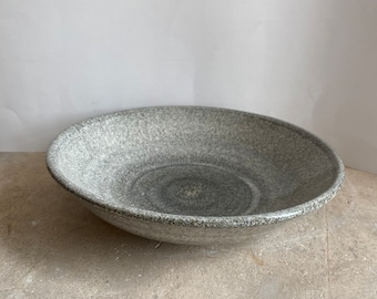 May include: A large, gray ceramic bowl with a speckled finish. The bowl has a wide, shallow shape and a slightly raised rim.