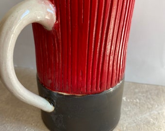 May include: A red and black ceramic mug with a white handle. The mug has a textured, ribbed design.