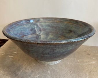 May include: A large, wide, ceramic bowl with a dark blue glaze and brown accents. The bowl has a slightly uneven rim and a speckled finish.