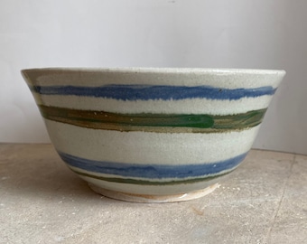 May include: A white ceramic bowl with blue, green, and brown stripes. The bowl is hand-painted and has a rustic, handmade look.