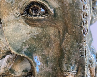 May include: Close-up of a ceramic elephant sculpture with a detailed eye and textured surface. The sculpture is painted in shades of green and brown.