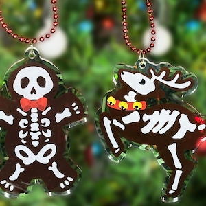 以下が含まれることがあります： スケルトンデザインのジンジャーマンとトナカイの形をしたクリスマスオーナメント2つ。オーナメントは透明なアクリル製で、赤と黄色のアクセントが施されています。