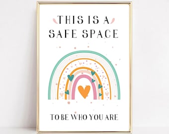 May include: A white framed print with a rainbow design and the text "This is a safe space to be who you are". The rainbow is made up of orange, yellow, pink, and green stripes with small hearts scattered throughout.