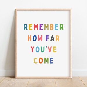 May include: A framed print with the text "REMEMBER HOW FAR YOU'VE COME" in colourful letters. The letters are in different colours, including red, orange, yellow, green, blue, purple, and pink.
