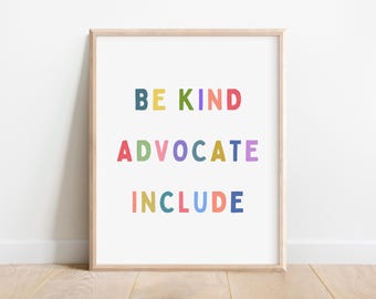 May include: A framed print with the words "BE KIND ADVOCATE INCLUDE" in colorful block letters. The text is centered on a white background, framed by a light wood border. The print is displayed against a white wall.