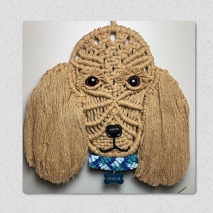 Może przedstawiać: Wiszący makramowy w kolorze beżowym w kształcie głowy psa z niebiesko-białym wzorzystym kołnierzem i etykietą z imieniem "CHARLIE".