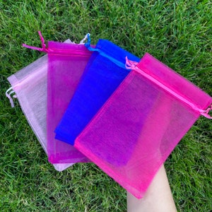 May include: Four sheer organza gift bags in pink, blue, and white. The bags are made of a delicate, translucent fabric and have a drawstring closure.