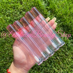 K&ouml;nnte beinhalten: Ein Set mit sechs transparenten Lipgloss-R&ouml;hrchen mit rosa Kappen und einem wei&szlig;en Applikator in Form eines Hirschfu&szlig;es. Die R&ouml;hrchen sind mit einer klaren Fl&uuml;ssigkeit gef&uuml;llt.