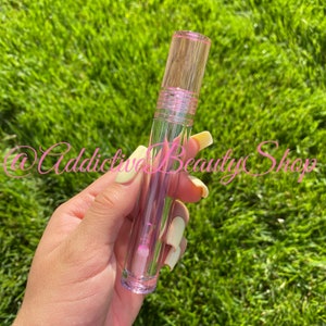 K&ouml;nnte beinhalten: Ein transparentes Lipgloss-R&ouml;hrchen mit rosa Deckel. Das R&ouml;hrchen ist mit einer klaren Fl&uuml;ssigkeit gef&uuml;llt.