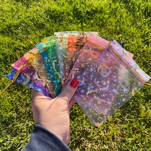 May include: A collection of colorful sheer organza bags with gold stars and crescent moon patterns. The bags are made of a delicate, translucent fabric and are perfect for packaging small gifts or favors.