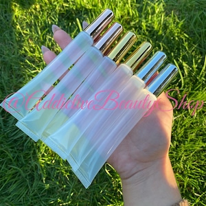 May include: A set of six clear lip gloss tubes with gold and silver caps. The tubes are arranged in a hand, with the caps facing the viewer.