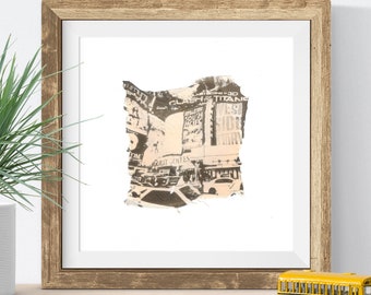 May include: A framed print of a torn piece of paper with a black and white photo of a city street scene. The photo shows a street with buildings and billboards with text that reads "Clash of the Titans 3D", "South Pacific", and "West Side Story".