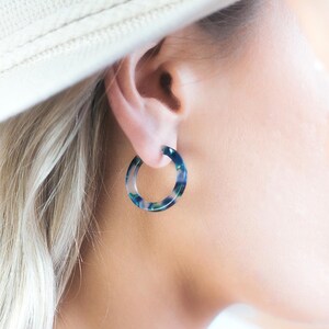 May include: A close-up of a blue and green marbled hoop earring. The earring is a circular shape and is worn on the ear. The earring is made of a translucent material.