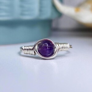 May include: A silver wire wrapped ring with a purple amethyst gemstone.