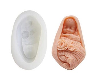 May include: A silicone mould and a finished resin casting of a sleeping baby wrapped in a blanket with flowers. The baby is pink and the blanket is a light peach colour.
