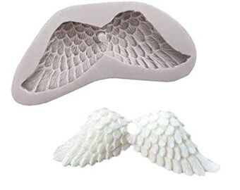 May include: A gray silicone mold shaped like angel wings, with detailed feather impressions. Below, two small, white, sculpted angel wings are displayed, showcasing a textured, layered design. Ideal for crafting and decorative projects.