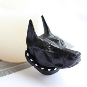 Op de afbeelding: Zwarte hars hondenkop sculptuur met een gespikkeld kraag. Het beeld is gedetailleerd en realistisch, met een textuur oppervlak.