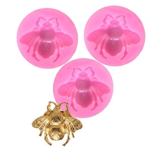 May include: Three pink silicone molds shaped like bees, with a gold bee charm.