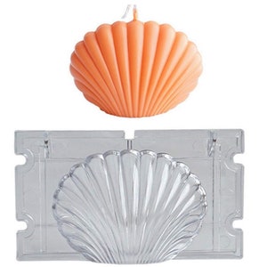 May include: An orange seashell-shaped candle is positioned above a clear plastic mould. The candle has a textured surface with a wick at the top. The mould is rectangular with a seashell design, ideal for crafting decorative candles.