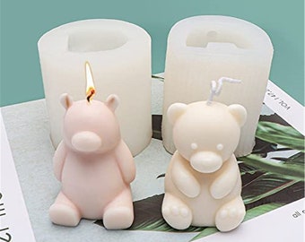 May include: Two silicone molds for making bear-shaped candles. One mold is pink and the other is white. Both molds have a small hole at the top for inserting a wick.