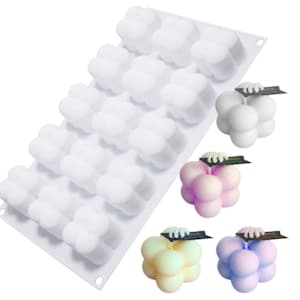 Könnte beinhalten: Weiße Silikonform mit 16 einzelnen Vertiefungen in Form einer Traube aus vier Kugeln. Die Form wird mit drei fertigen Kerzen in verschiedenen Farben gezeigt: weiß, rosa und hellblau.