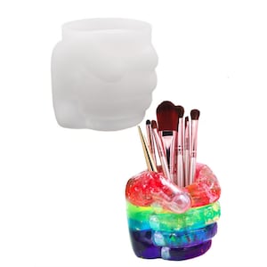 Op de afbeelding: Een regenboogkleurige harshand in de vorm van een vuist met een set make-upkwasten erin. De hand is een decoratieve houder voor make-upkwasten.