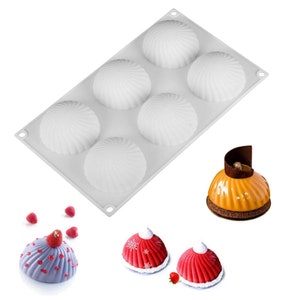 Op de afbeelding: Een witte siliconen mal met zes halfronde holtes, elk met een spiraalvormig ontwerp. De afbeelding toont ook afgewerkte desserts in verschillende kleuren, waaronder oranje, rood en grijs, versierd met fruit.