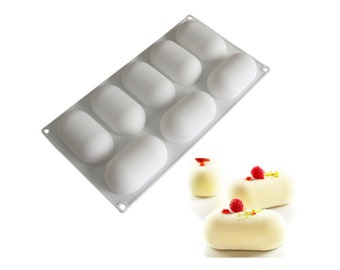 May include: White silicone mould with eight oval-shaped cavities. The mould is designed for making small cakes or desserts.