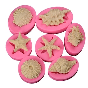 May include: Pink silicone moulds for baking or crafting, featuring various sea life designs: starfish, seashells, and a sea urchin.