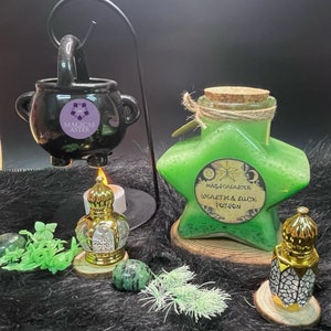 May include: A green star-shaped glass bottle with a cork stopper and a label that reads "MagicaeAster Wealth & Luck Potion". The bottle is sitting on a brown surface with a black cauldron, a gold candle holder, and green plants.