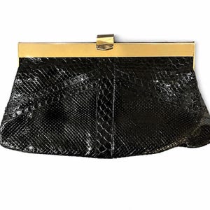 Può includere: Una pochette nera con motivo a pelle di serpente. La borsa rettangolare ha una cornice e una chiusura color oro. Un accessorio classico per serate o occasioni speciali.