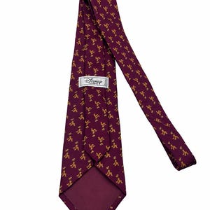 May include: A deep burgundy necktie featuring a repeating pattern of small, yellow Pluto character silhouettes. The tie includes a white rectangular label on the back with the black text Disney Fashions printed in a stylised font.