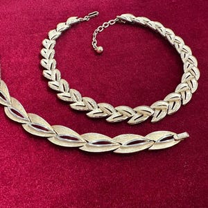 Puede incluir: Un conjunto de collar y pulsera de metal en tono dorado con un diseño de eslabones en forma de hoja. Las piezas de joyería tienen un acabado mate cepillado con detalles en tono plateado pulido en el centro de cada eslabón de hoja.