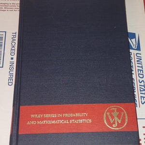 May include: A dark blue hardcover book with a horizontal red band across the lower portion. The text reads Wiley Series in Probability and Mathematical Statistics, accompanied by a circular gold logo featuring the letters JW in the center.