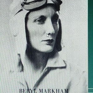 May include: Black and white portrait of Beryl Markham, a female aviator, wearing a leather helmet and goggles. The text "BERYL MARKHAM" is printed below the image.
