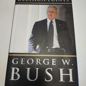 May include: A black hardcover book with the title "Decision Points" and the author's name "George W. Bush" in white lettering. The cover features a photo of George W. Bush in a suit and tie, standing in front of a white building.