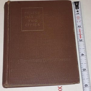 May include: A brown hardcover book titled "Dickens Tale of Two Cities" from Macmillan's Pocket Classics. The book is approximately 5 inches tall. The cover has embossed text and a slightly worn appearance.