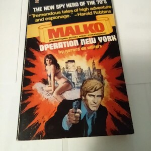 May include: A paperback book cover with a red, yellow, and black color scheme. The title is "Operation New York" and the author is "Gerard de Villiers". The cover features a man holding a gun and a woman in a bikini.