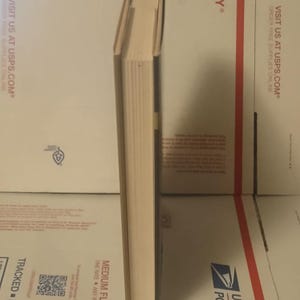 K&ouml;nnte beinhalten: Ein Hardcover-Buch, das vertikal auf seiner Unterkante steht und den Buchr&uuml;cken sowie die cremefarbenen Seitenkanten zeigt. Das Buch hat einen dunkelbraunen Einband und ein schlichtes, klares Design ohne sichtbaren Text oder Grafiken.
