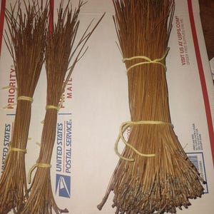 May include: Three bundles of dried, golden-brown pine needles. Two smaller, thinner bundles are tied with yellow string, while one larger, thicker bundle is also secured with yellow string. The needles are long, slender, and pointed.