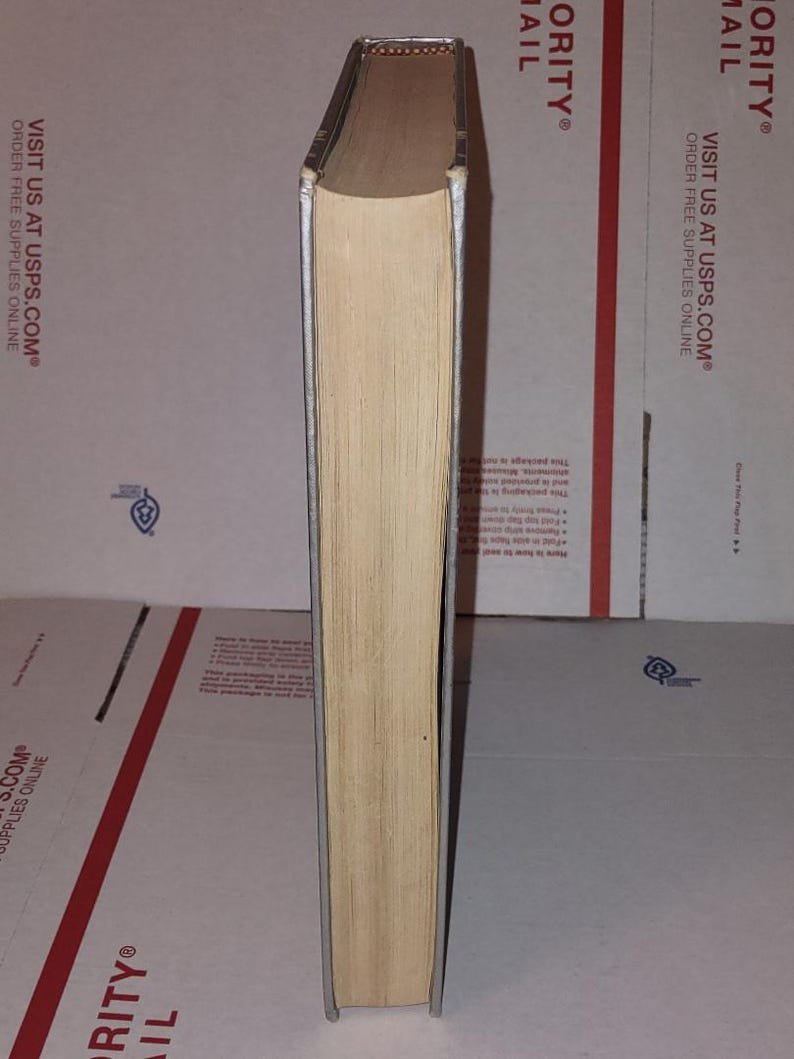 Puede incluir: Un libro de tapa dura con lomo de color beige claro y bordes plateados. Las p&aacute;ginas son de color beige claro. El libro est&aacute; de pie sobre un fondo neutro.