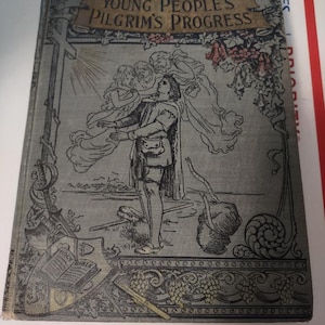 May include: A vintage book cover with a blue background and a gold banner that reads "Young People's Pilgrim's Progress". The cover features a black and white illustration of a man holding a woman in his arms, surrounded by angels.
