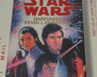 May include: A Star Wars novel titled "Darksaber" by Kevin J. Anderson. The cover features a colorful illustration of Luke Skywalker, Princess Leia, and Han Solo with lightsabers. The background is a dark space scene with stars.