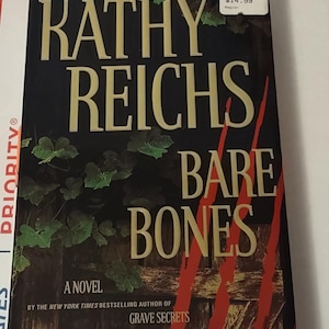 May include: A paperback novel titled "Bare Bones" by Kathy Reichs, the New York Times bestselling author of "Grave Secrets". The cover features a dark green and brown background with red claw marks.