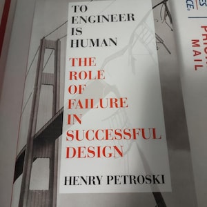 May include: A book titled "To Engineer Is Human: The Role of Failure in Successful Design" by Henry Petroski. The cover features a black and white photo of the Golden Gate Bridge.